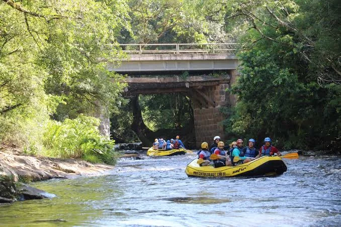 Botes de rafting descendo o Rio Paranhana sob uma ponte de pedra, no Parque das Laranjeiras