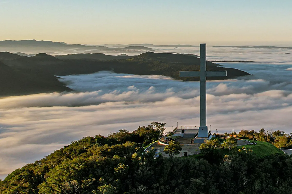 A cruz do Monte da Fé no alto do morro, sobre um mar de nuvens ao amanhecer