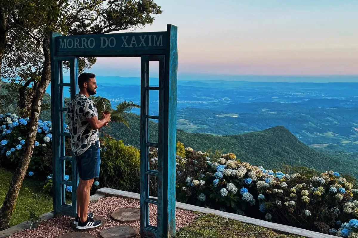 O portal de madeira do Morro do Xaxim, com hortênsias e a vista do vale ao entardecer